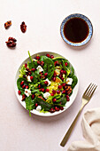 Top view of delectable winter salad is garnished with candied walnuts, pomegranate seeds, assorted lettuces, crumbled goat cheese, cranberries, and a unique olive oil, Modena vinegar