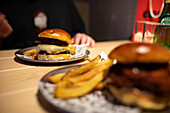 Nahaufnahme eines köstlich saftigen Cheeseburgers mit schmelzendem Käse und goldenen Pommes frites, serviert auf modernem Geschirr in einem gemütlichen Restaurant