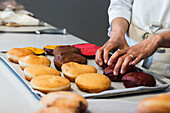 Crop faceless baker putting sweet sponge cakes on tray while preparing vegan desserts in kitchen of bakery