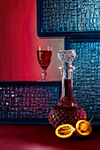 A crystal decanter with rich reddish-brown bitter tamarind beverage, complemented by a matching glass against a red and blue textured backdrop