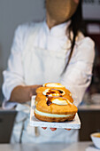 Anonymous crop baker standing with sweet vegan Berliners with sugar crust on board in bakehouse