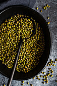 A rustic display of raw organic mung beans heaped in a dark skillet, with a black spoon partially filled