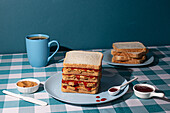 Stapel Erdnussbutter-Gelee-Sandwiches auf einem blauen Teller, mit einer Tasse amerikanischem Kaffee und einigen Brotscheiben auf blauem Hintergrund