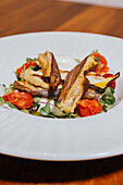 Roasted eggplant and cherry tomatoes artfully arranged on a bed of greens, creating a visually appealing gourmet salad