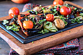 A vibrant display of grilled vegetables including bell peppers, mushrooms, and eggplants, garnished with fresh parsley and served on a dark wooden cutting board