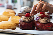 Crop unrecognizable baker decorating Berliners with whipped cream and with raspberries placed on table in bakery