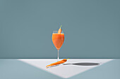 Elegantly presented fresh carrot juice in a wine glass, with a whole carrot as garnish, against a soft blue background.