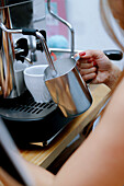 A close-up view of a hand steaming milk in a metallic jug using a professional coffee machine, perfect for cake recipes