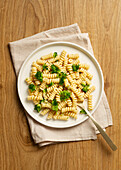 Top view of plate of cooked fusilli pasta topped with fresh broccoli florets, served on a wooden table with a linen napkin