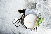 A fresh, mint-themed table setting for summer featuring a rustic plate tied with twine, a sprig of mint, elegant cutlery, and a textured glass on a speckled surface