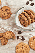 Chocolate chip cookies in a glass bowl and scattered on a rustic wooden table, photographed from above