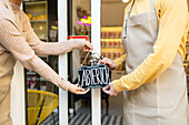 Two individuals hang the 'Abierto' (Open in Spanish) sign on the door, signaling the start of a business day.