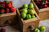 Vintage wooden drawers filled with fresh organic strawberries, sweet cherries, and green plums, presented in a rustic, natural setting with a focus on healthy, farm-fresh produce