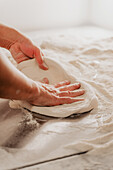 An anonymous chef in a pizzeria presses and shapes pizza dough on a flour-dusted surface in a cropped, faceless photograph