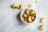 A close-up view of withered roses in a bowl, elegantly staged against a textured gray background The dried flowers convey a sense of timeless beauty and subtle grace, perfect for themed decorations or nostalgic compositions