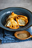 A beautifully presented trio of golden-brown Georgian khinkali, served on a rustic ceramic plate, accompanied by pepper seasoning