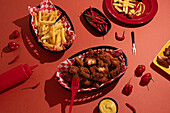 A tempting spread of crispy fried chicken pieces and golden fries in checkered baskets, accompanied by fresh red chili peppers, all set on a vibrant red background