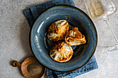 A close-up view of traditional Georgian khinkali dumplings on a textured blue ceramic plate, accompanied by a wooden scoop of spices and a clear wine glass, set against a gray tabletop