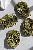 Top view of green spinach pasta nests arranged neatly on a white marble surface, illuminated by natural light