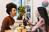 Side view of cheerful woman feeding black female friend with poke while chilling in restaurant together