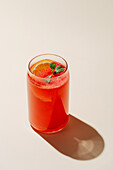 Vibrant berry-orange lemonade in a glass, garnished with fresh mint and a slice of orange, perfect for a hot day.