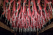 Traditional Sobrasada sausages from the Balearic Islands, known for their vibrant red color from paprika, hanging neatly on hooks in a dimly lit curing room to dry and develop flavor.