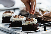 Unbekannter Erntekoch bestreut appetitlichen veganen Biskuitkuchen mit Schokolade, während er in der Küche einer Bäckerei kocht