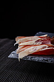 A close-up image showcasing thin slices of authentic Serrano ham, elegantly arranged on a dark, textured slate plate This scene captures the essence and richness of typical Spanish cuisine