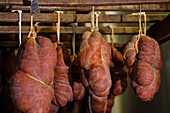 Selection of cured meats, with a focus on Sobrasada sausages, traditionally made from pork and spices, suspended in a shop under warm lighting.