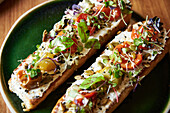 Close-up of freshly prepared bruschetta with vibrant toppings on a dark green plate, showcasing a blend of flavors and colors for an inviting meal.