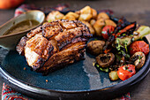 Succulent baked pork covered in a rich honey sauce, accompanied by a colorful salad of grilled vegetables, including tomatoes and mushrooms, served on a dark ceramic plate