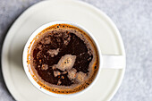 Top view of a steamy, freshly brewed cup of coffee in a white mug, placed on a matching saucer on a textured surface.