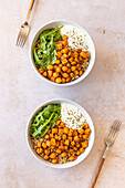 Two bowls of quinoa salad topped with roasted sweet potatoes and spiced chickpeas served with a dollop of yogurt sauce