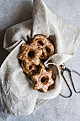 From above, homemade gingerbread cookies shaped like stars are nestled in a natural linen cloth, evoking a cozy, rustic ambiance. The cookies are dusted with sugar, offering a textural contrast to the soft folds of the fabric.