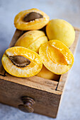 Bright yellow nectarines, both whole and halved, are neatly arranged in a rustic wooden drawer, displaying their vibrant, juicy flesh and central pits