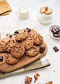 A delicious selection of chocolate chip cookies on a wooden board, accompanied by chocolate chunks, a milk jar, sugar bowl, in the background Perfect for dessert and snack concepts