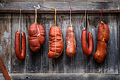 Traditional cured meats including Sobrasada and various sausages hanging from strings against a textured wooden backdrop, showcasing a rustic culinary scene.