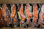 A selection of traditional cured meats, prominently featuring Sobrasada, is displayed hanging at a local market. These meats are seasoned primarily with spices such as paprika and salt.