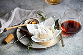 A sophisticated setup featuring Brie cheese on a plate, paired with a glass of red wine, complete with a honey dipper and rosemary.