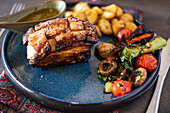 Crispy baked pork ribs generously drizzled with a honey sauce, accompanied by a salad of colorful grilled vegetables on a ceramic plate