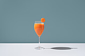 An elegant glass filled with vibrant orange carrot juice, garnished with a fresh carrot slice placed on the rim, set against a soft blue background.