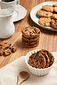 A top view of tasty chocolate chip cookies on a wooden table, accompanied by white ceramic dishware