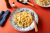 A close-up shot of fettuccine Alfredo on a red background. Garnished with fresh parsley and grated Parmesan cheese