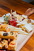 Ein Holzbrett mit einer Reihe von handwerklich hergestellten Käsesorten, Focaccia-Scheiben und einem Glas Beerenmarmelade ist der Inbegriff eines Gourmet-Snacks