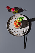 Top view of a vibrant salad served in a transparent glass, artistically set on a gray background with olive oil bottles and a metal fork.