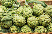 A close-up of vibrant green artichokes piled in a woven basket, fresh from the farmers market