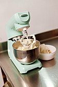 A mint green stand mixer whips cream in a stainless steel bowl, essential for baking cakes, with ingredients nearby