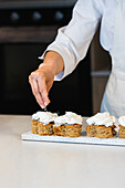 Crop anonymous cook sprinkling vegan carrot cakes while preparing desserts in bakery