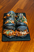 Gourmet sliders with succulent fillings and charcoal buns, adorned with fresh microgreens on a sleek black serving platter