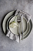 Top view a refined table setting featuring layered ceramic plates and a soft gray napkin, accentuated by a delicate godetia flower lying gently across the setup